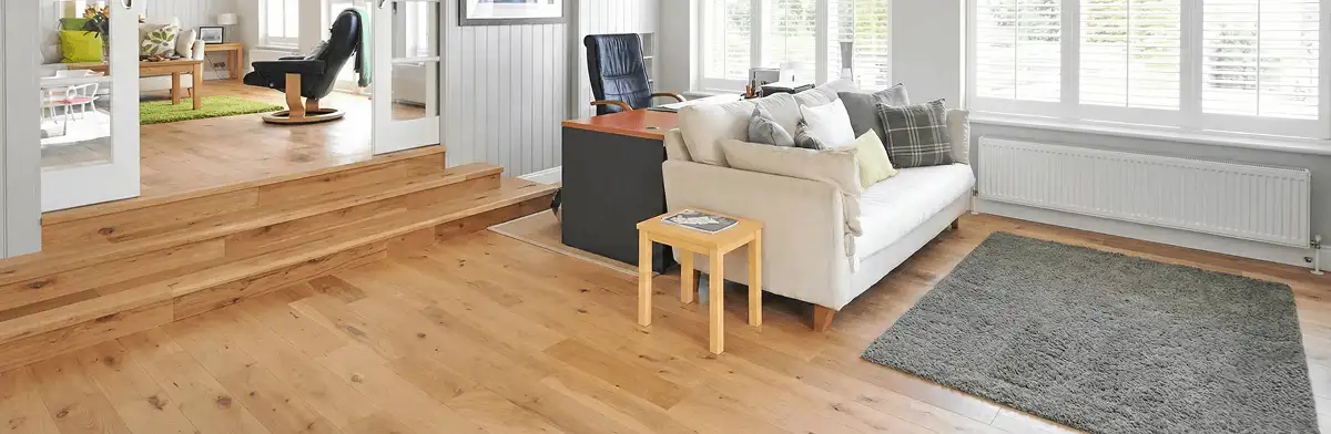 A modern living room with professionally installed laminate flooring, a beige sofa, a small side table, a gray rug, and large windows with white shutters in Baltimore, MD